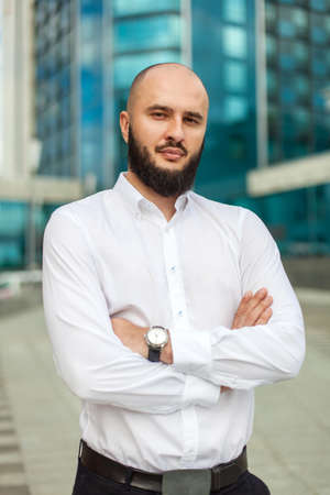 Businessman with beard in white shirt standing near office buildingの写真素材