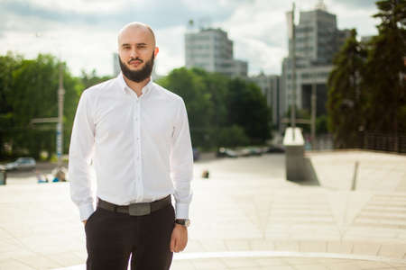 Businessman with beard in white shirt standing in modern cityの写真素材