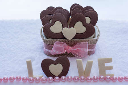 Pretty Rolled Vanilla Heart inside Chocolate Heart Sugar Cookies in a Ceramic bowl wraps with Burlap and the word LOVE Cookies and pink pearlsの写真素材