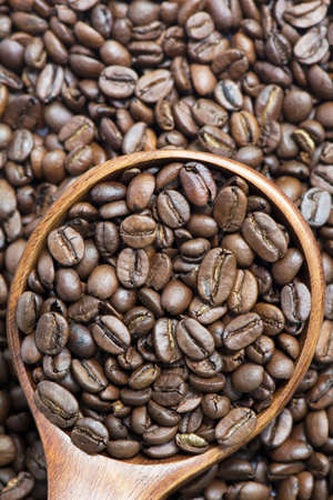 Medium roasted whole coffee bean in wooden spoon on coffee bean backgroundの写真素材