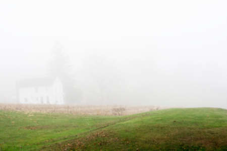 Small green grass hill with a blur farm house in a foggy morning backgroundの写真素材