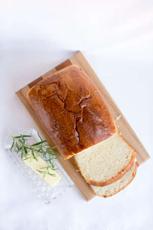 Delicious slices of  homemade white bread loaf on wood cutting board with butter and rosemary on...