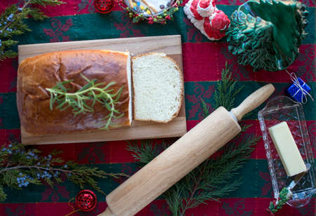 Delicious homemade white bread loaf on wood cutting board with butter and rosemary, Christmas bread set up on fabric table cloth for holiday dinnerの写真素材