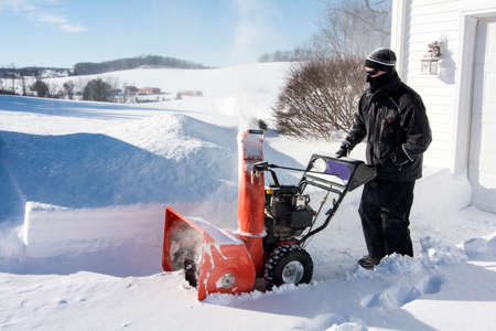 Close up of  man in black dress using a snow blower plowing snow after Jonas snow storm in the morningの写真素材