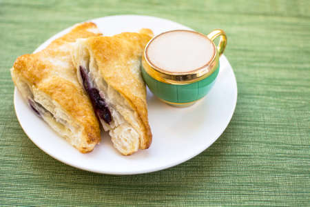 Mini cup of cappuccino and two pieces blueberry cobbler puff pastries on white plate and green placemat background, Cobbler puff pastries breakfast and a cup of coffeeの写真素材
