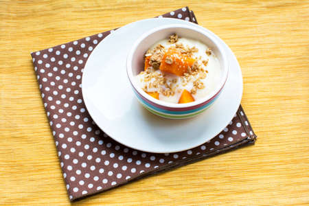 Healthy pumpkin yogurt dessert with maple granola topping, Healthy pumpkin snack bowl on yellow placematの写真素材