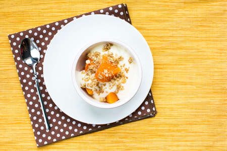 Healthy pumpkin yogurt dessert with maple granola topping, Healthy pumpkin snack bowl on yellow placemat, Above shot food photographの写真素材