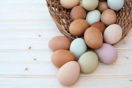 Colorful fresh organic chicken eggs overflow out of old dusty basket on wooden background, Colorful natural chicken eggs, Selected focus organic chicken eggs overflow out of the basketの写真素材
