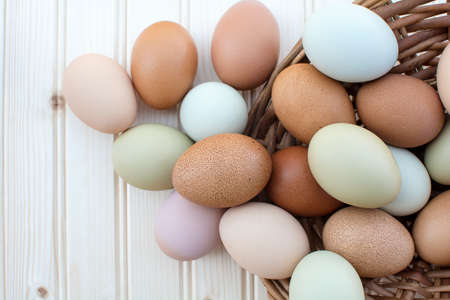 Colorful fresh organic chicken eggs overflow out of basket on wooden background, Colorful natural chicken eggs, Selected focus organic chicken eggs overflow out of the basketの写真素材