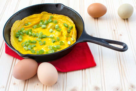 Omelette garnished with green onions in cast iron skillet on wood background, Tasty omelette breakfastの写真素材