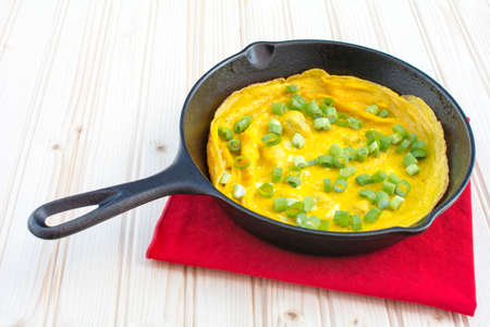 Omelette garnished with green onions in cast iron skillet on wood background, Tasty omelette breakfastの写真素材