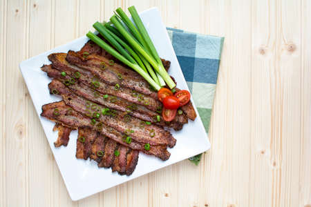 Above shot of oven baked peppercorn bacon garnish with chopped green onions with tomato and green onion on wood backgroundの写真素材