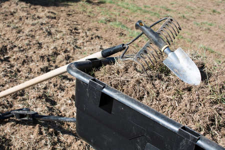 Dirty gardening tools on pile of dirt and grasses in black plastic yard cart, tools and dirts in wheelbarrowの写真素材