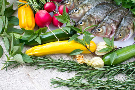 Cut and cleaned fresh perch fish on white cutting board with fresh organic vegetables on burlap backgroundの写真素材