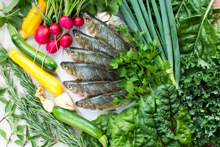 Cut and cleaned fresh perch fish on white cutting board with fresh organic vegetables on burlap backgroundの写真素材