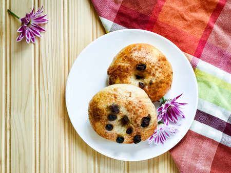 Two pieces of homemade organic cinnamon raisin bagels on white round plate decorated with purple flowers on plaid napkin and wood background.の写真素材