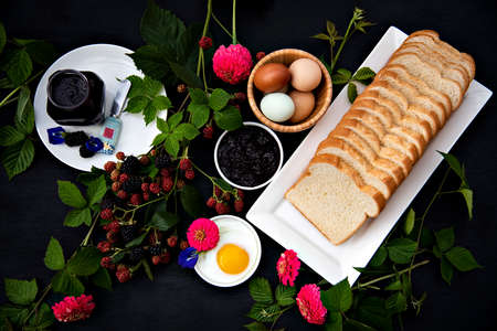 Breakfast set up, Selective focus, homemade organic blackberry jam, hard boiled eggs, fried egg, sliced bread loaf decorated with fresh blackberry branches, pink zinnia and blue butterfly pea  flowers.の写真素材