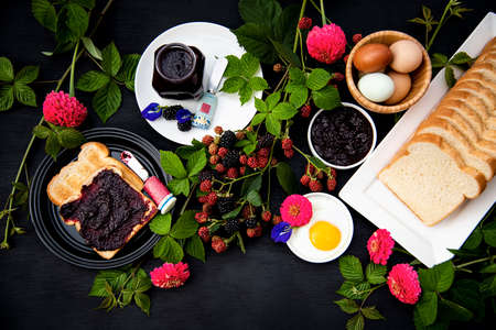 Breakfast set up, Selective focus, Toasted spread with homemade organic blackberry jam, hard boiled eggs, fried egg, bread decorated with fresh blackberry branches, pink zinnia and blue butterfly pea  flowers.の写真素材