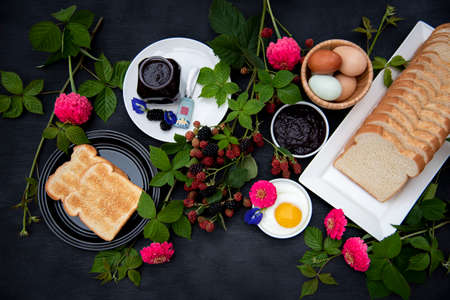 Breakfast set up, Selective focus, Toasted, homemade organic blackberry jam, hard boiled eggs, fried egg, bread decorated with fresh blackberry branches, pink zinnia and blue butterfly pea  flowers.の写真素材