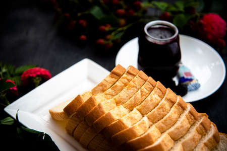 Selective focus of sliced bread  loaf on a white plate with homemade organic blackberry jam jar, fresh blackberry branches, pink zinnia and blue butterfly pea  flowers as a background.の写真素材
