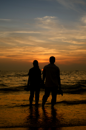 Couple of woman and man staying near sea and looking at sunsetの写真素材