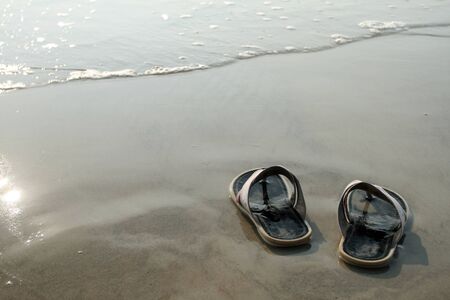 black slippers standing on the wet sand near the waterの写真素材