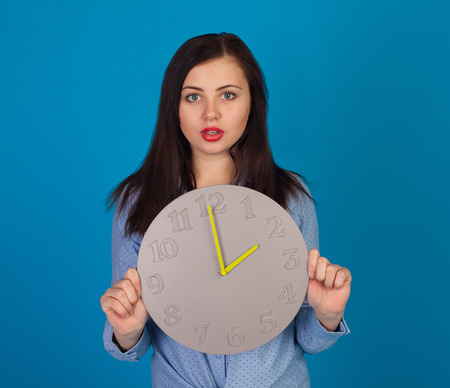 Surprised woman with grey clock in her hands is standingの写真素材