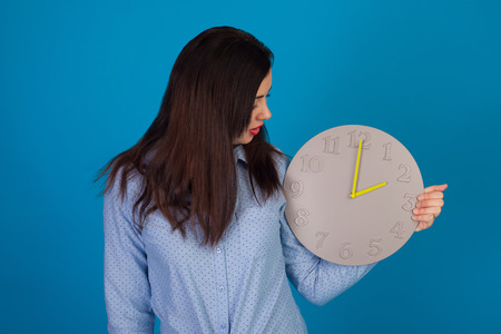 Cute woman with grey clock in her hand is standing