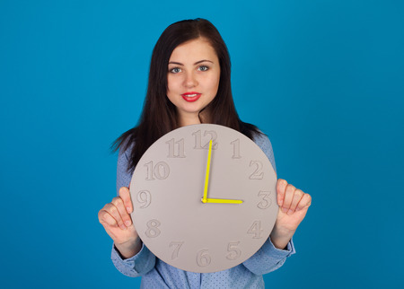 Cute woman with clock in her hands is standing against of blue background