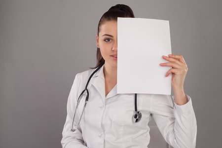 Nurse is hidding her face with a paper against of grey background