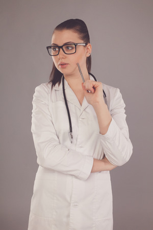 Nurse in white robe and glasses is looking somewhere against of grey backgroundの写真素材