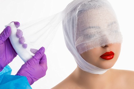The doctor with violet gloves is binding up with a bandage the woman with red lips 	
against the white background.の写真素材