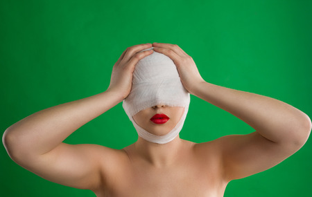 The woman with a bandage on her head and with full red lips is taking her head against the background of chromakey.の写真素材