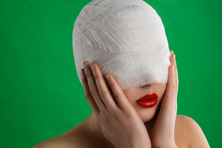 The woman with a bandage on her head and with full red lips is taking her face against the background of chromakey.の写真素材