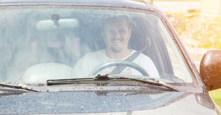 Young smiling man in white T-shirt driving the carの写真素材