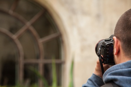Young man in blue shirt holding black camera and taking photoes of old building with big windowの写真素材