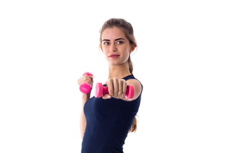 Sportive young woman in blue T-shirt holding pink dumbbells in her hands on white background in...