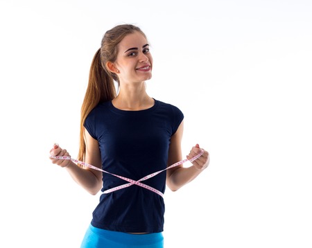 Young athletic woman in blue T-shirt and leggings measuring her waist with centimeter on white...