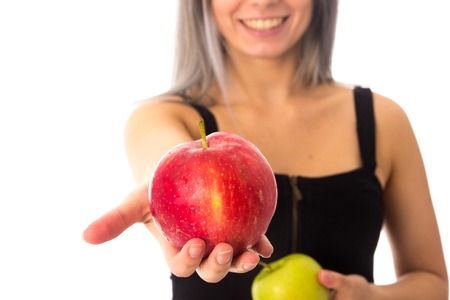 Young smiling woman in black top showing red apple on white background in studioの写真素材