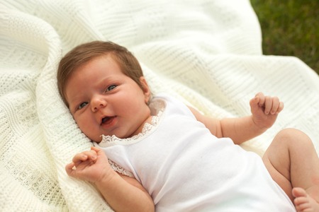 Charming little baby in white clothing on the white blanket on the grassの写真素材