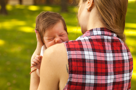 Young woman in checkered blouse holding little crying baby in the green parkの写真素材