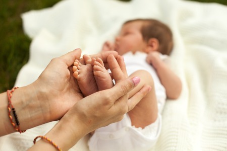 Hands holding legs of little sleeping baby on white blanket on the grassの写真素材