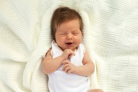 Little charming baby in white clothing lying and yawing on the white blanket