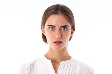 Young beautiful woman in white blouse looking scared and frightened on white background in studioの写真素材