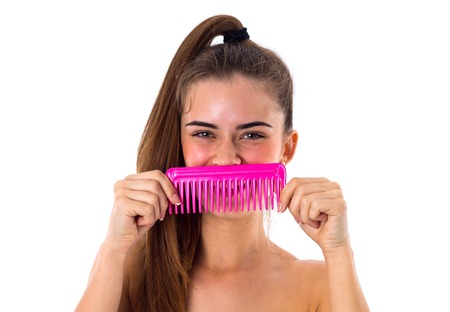 Young smiling woman with long brown ponetail holding pink hair brush on white background in studioの写真素材