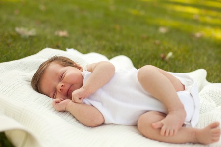 Little beautiful baby in white clothing sleeping on the white blanket on the grassの写真素材