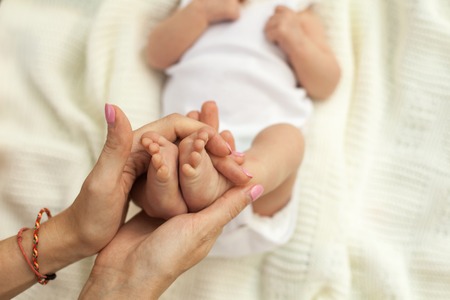 Hands holding legs of little sleeping baby on white blanketの写真素材