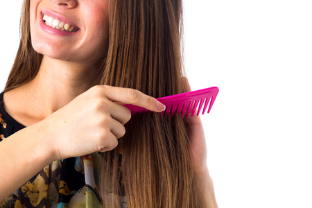 Young happy woman in colored shirt combing her long brown hair using pink hair brush on white background in studioの写真素材
