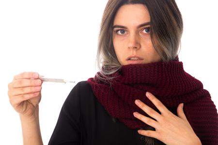 Young woman in black shirt with vinous long scarf holding a thermometer and looking at it on white background in studioの写真素材