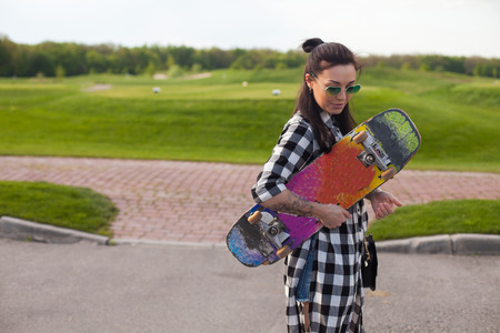 The woman in glasses is standing with an old skate in her hand on the background of park.の写真素材